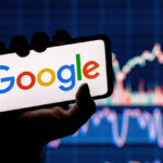 Una persona sostiene un smartphone en el que aparece el logotipo de Google Gemini Era, con un fondo borroso de gráficos bursátiles.