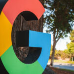 D Buchstabe 'G', der dem Google-Logo ähnelt, färbt draußen in einem parkähnlichen Setting. Kein konkreter Standort angegeben, möglicherweise in der Nähe des Google-Büros oder Campus.